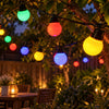 Multicolor LED garden string lights with round globe bulbs hanging on a tree in an outdoor backyard setting at dusk.