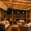 Black mesh pendant lights hanging under a wooden pergola on a cozy outdoor patio at night with warm Edison bulb glow and festoon lighting.