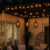 Outdoor patio with string lights, hanging chair, and cushions under a wooden pergola.