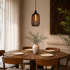 Dining room with a wooden table set for four, a vase with plants, and a hanging light fixture.
