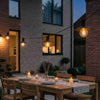 Elegant alfresco dining area illuminated by vintage black shade outdoor string lights against a brick courtyard.