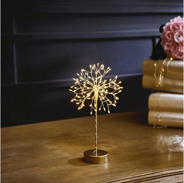 Gold dandelion table lamp with warm white LED lights on a wooden table in an interion setting.