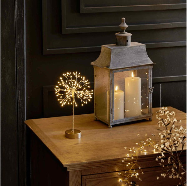 Gold dandelion LED table lamp glowing on a bedside r console table.