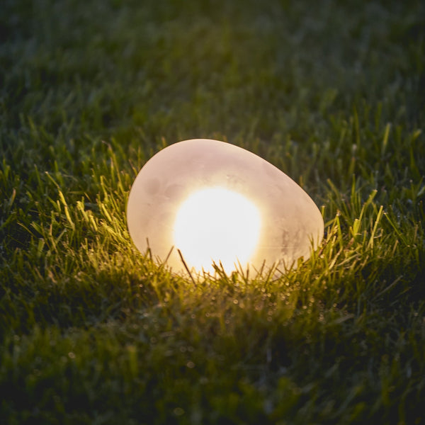 Warm white glow-in-the-dark decorative garden pebble light nestled in green lawn.